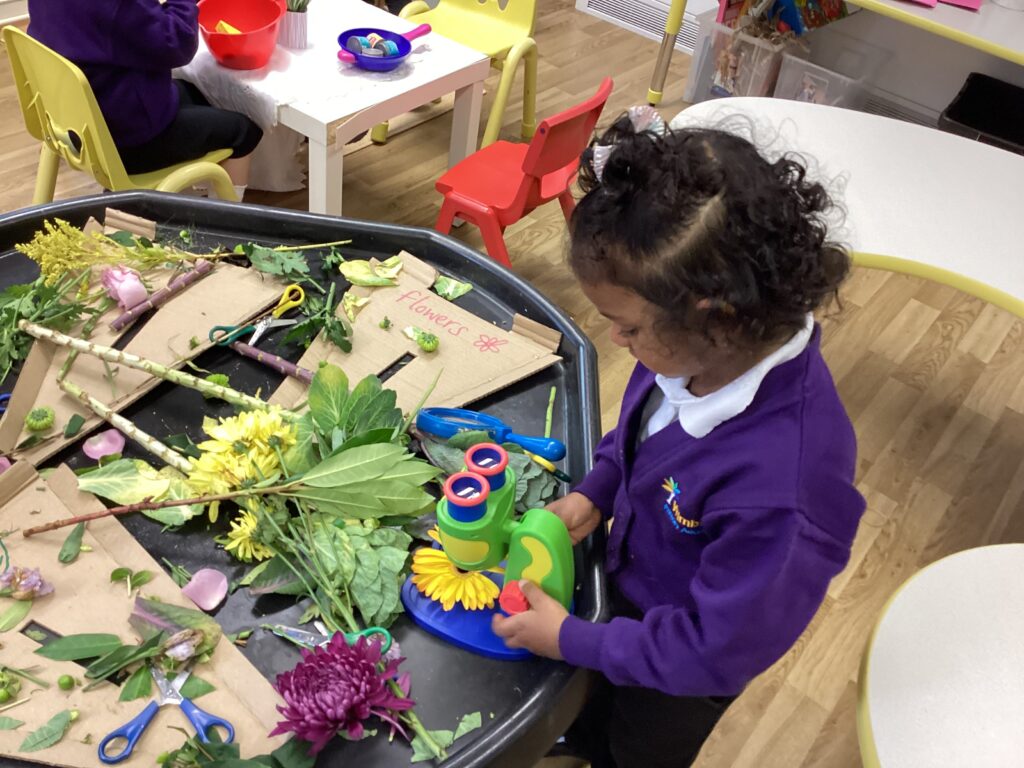 A pupil is sitting at a table and is putting a flower arrangement together. They are wearing a purple jumper with a white collar.