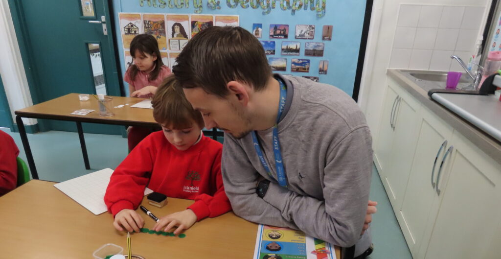 A teacher and child sitting at a desk looking at a small learning toy.