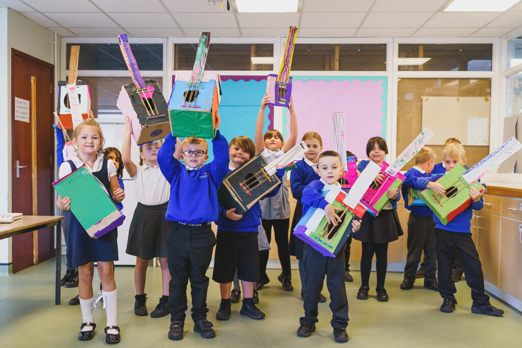 A group of pupils holding up painted guitars made of cardboard.