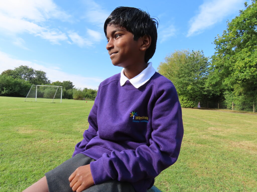 A pupil sitting on a bench smiling away from the camera.