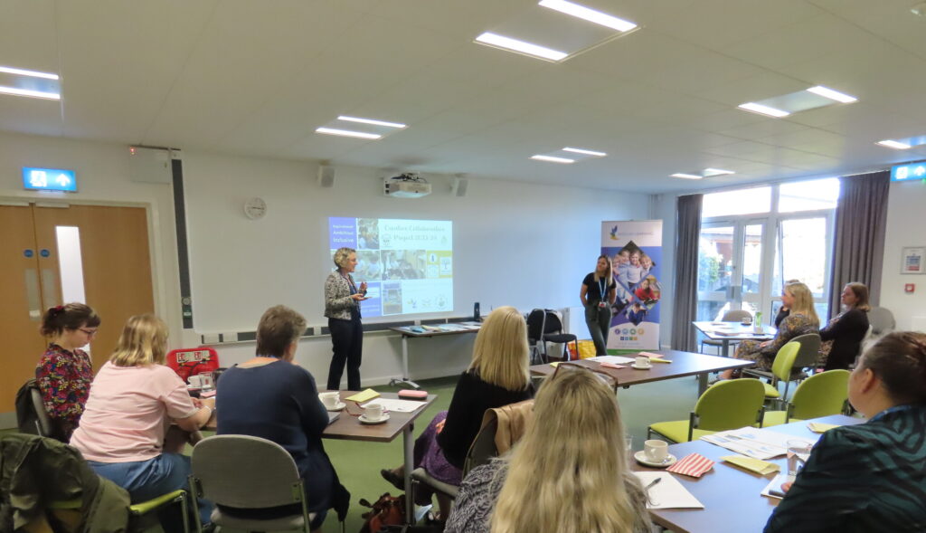 A person presenting to a group of people sat at a number of tables.