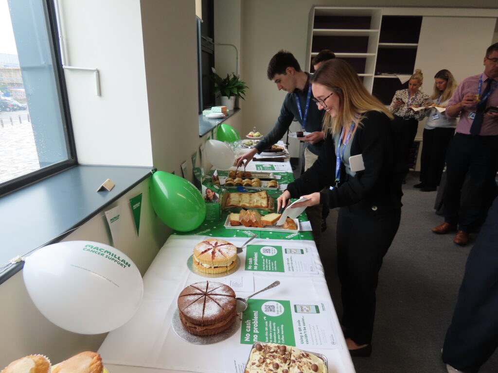 Two people cutting a slice of cake which is presented on a long table. 