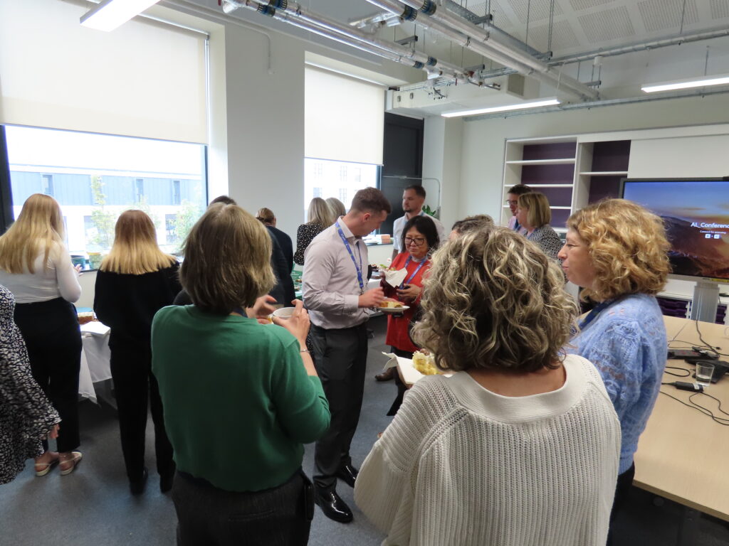 A group of people standing and eating cake whilst having a conversation.