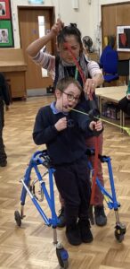 A young disabled child is holding a bow and arrow with the assistance of an adult