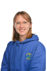 A white woman who is wearing a blue jumper and glasses is smiling at the camera