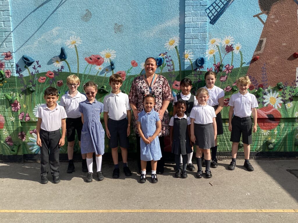 A woman is standing with a group of pupils who are all smiling towards the camera. The pupils are wearing school uniform.