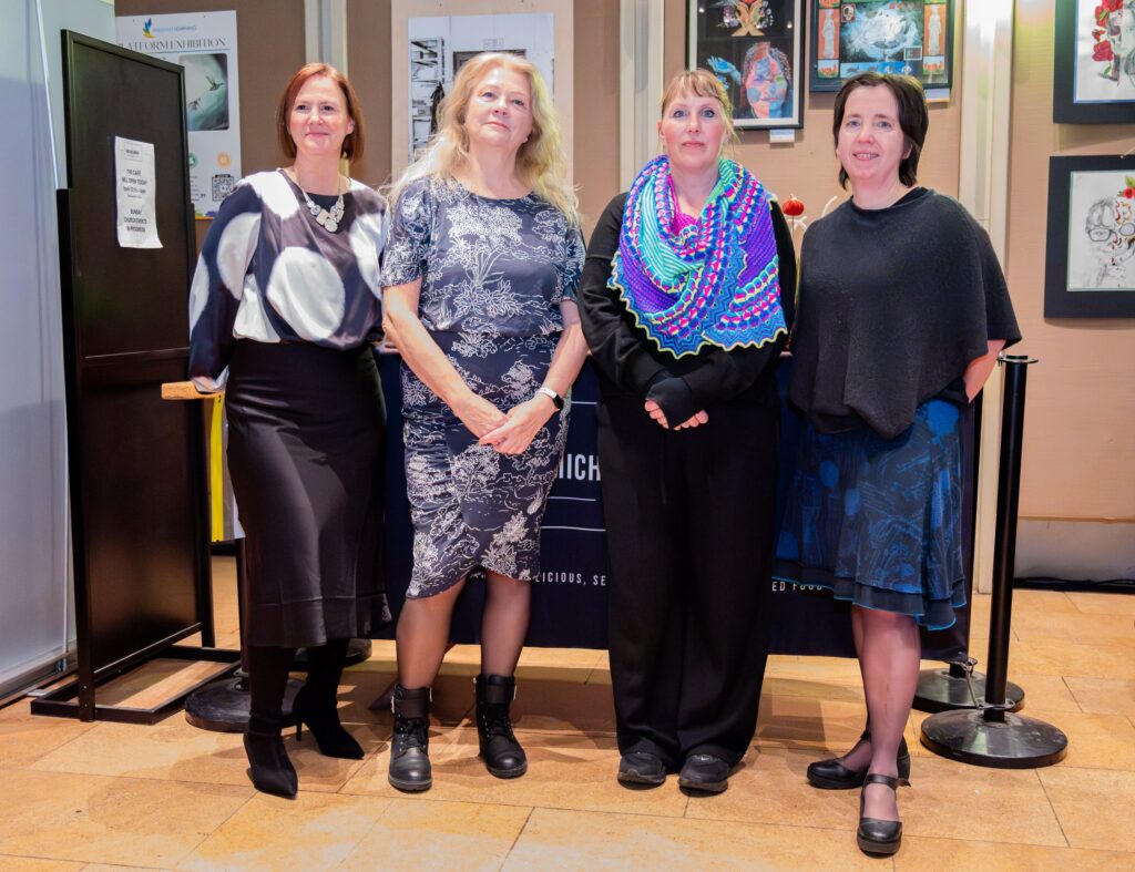 Four women are standing in front of artwork hung on a wall. 
