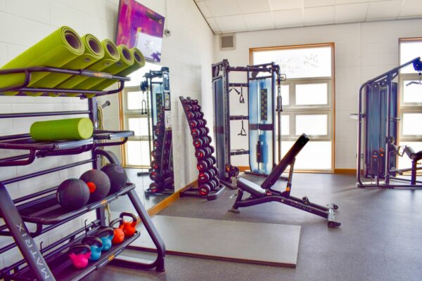 Exercise equipment including dumbells, yoga mats, and weight lifting machines inside the gym.