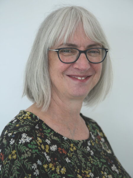 photograph of a lady with short grey hair and glasses smiling at the camera