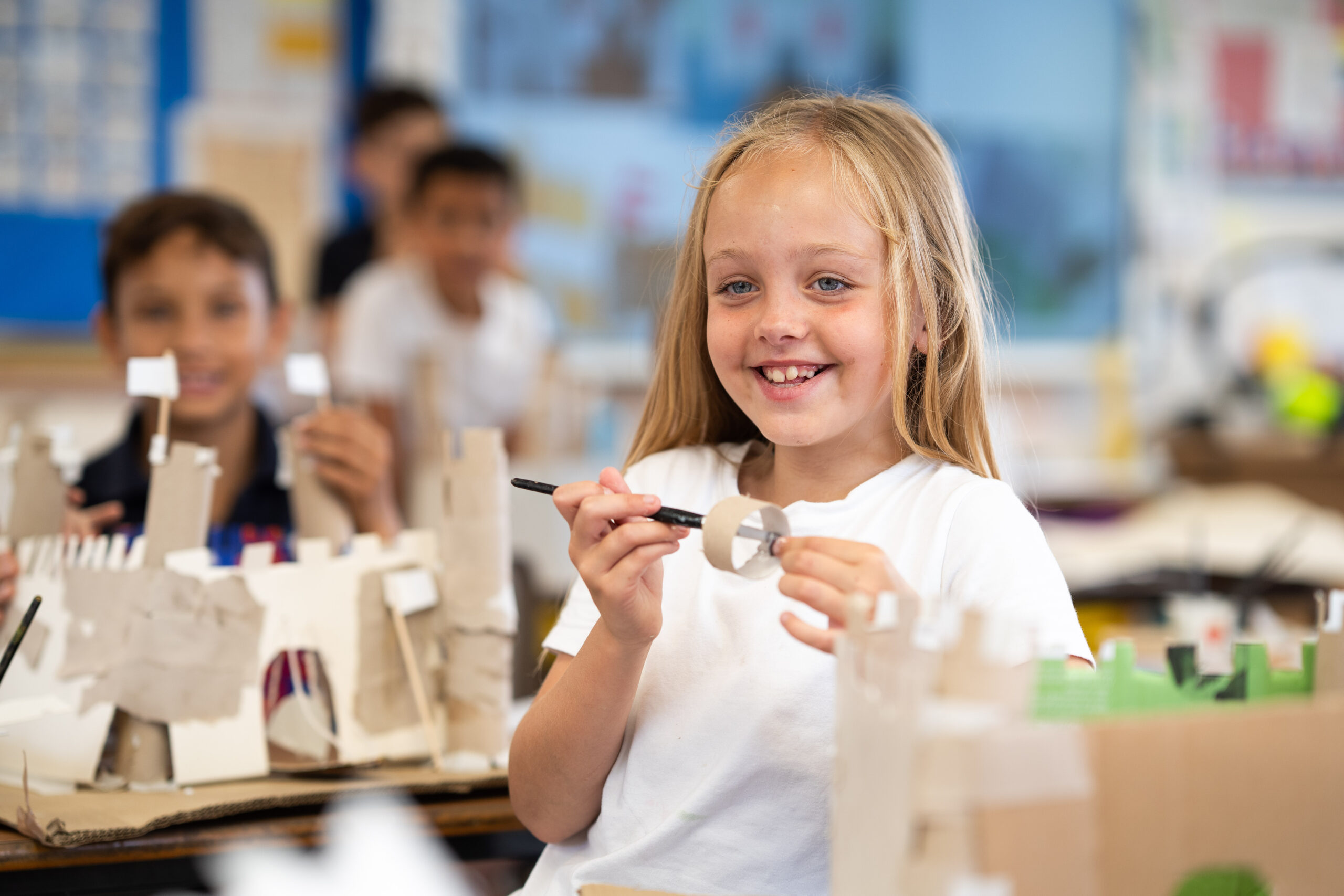 A young girl is smiling at the camera whilst holding a pen up.