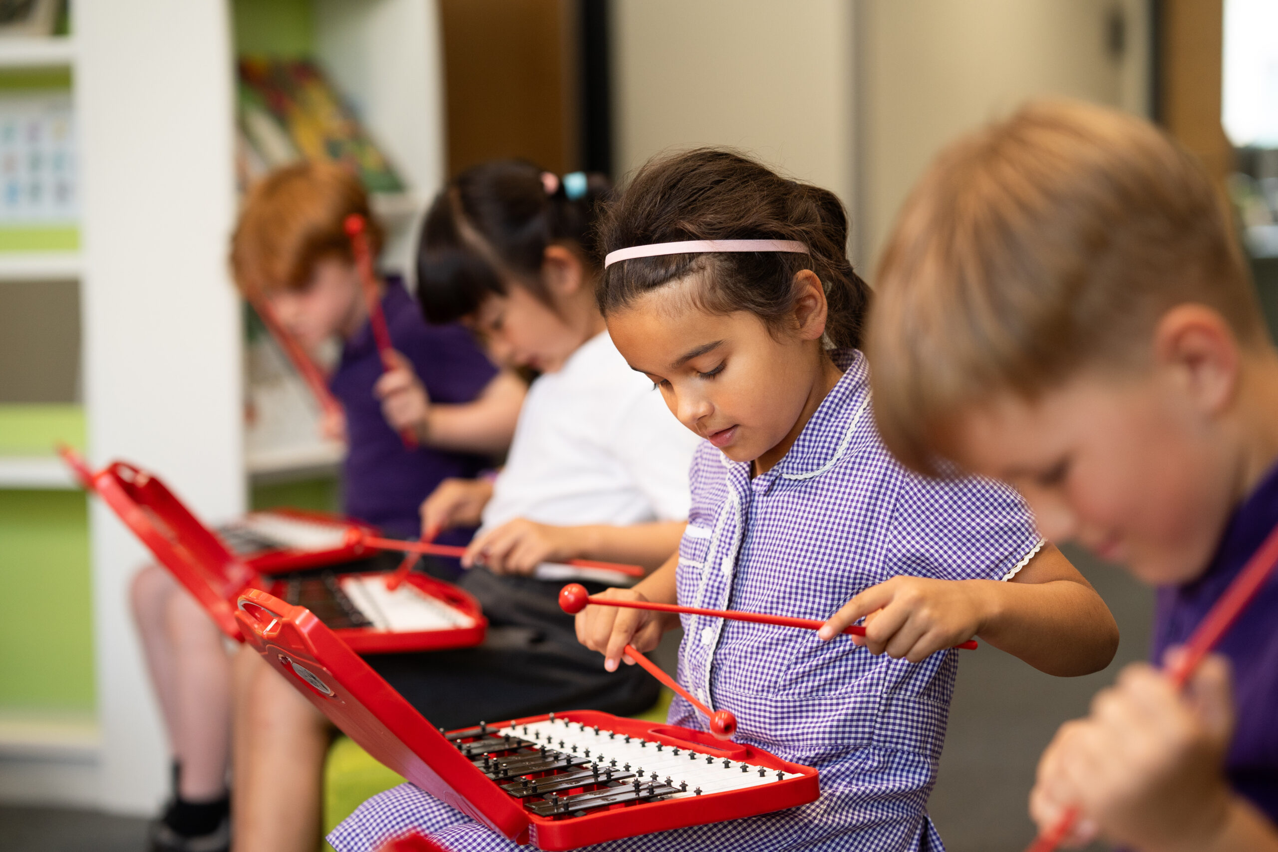 Four pupils have red Xylophones on their laps which they are playing.
