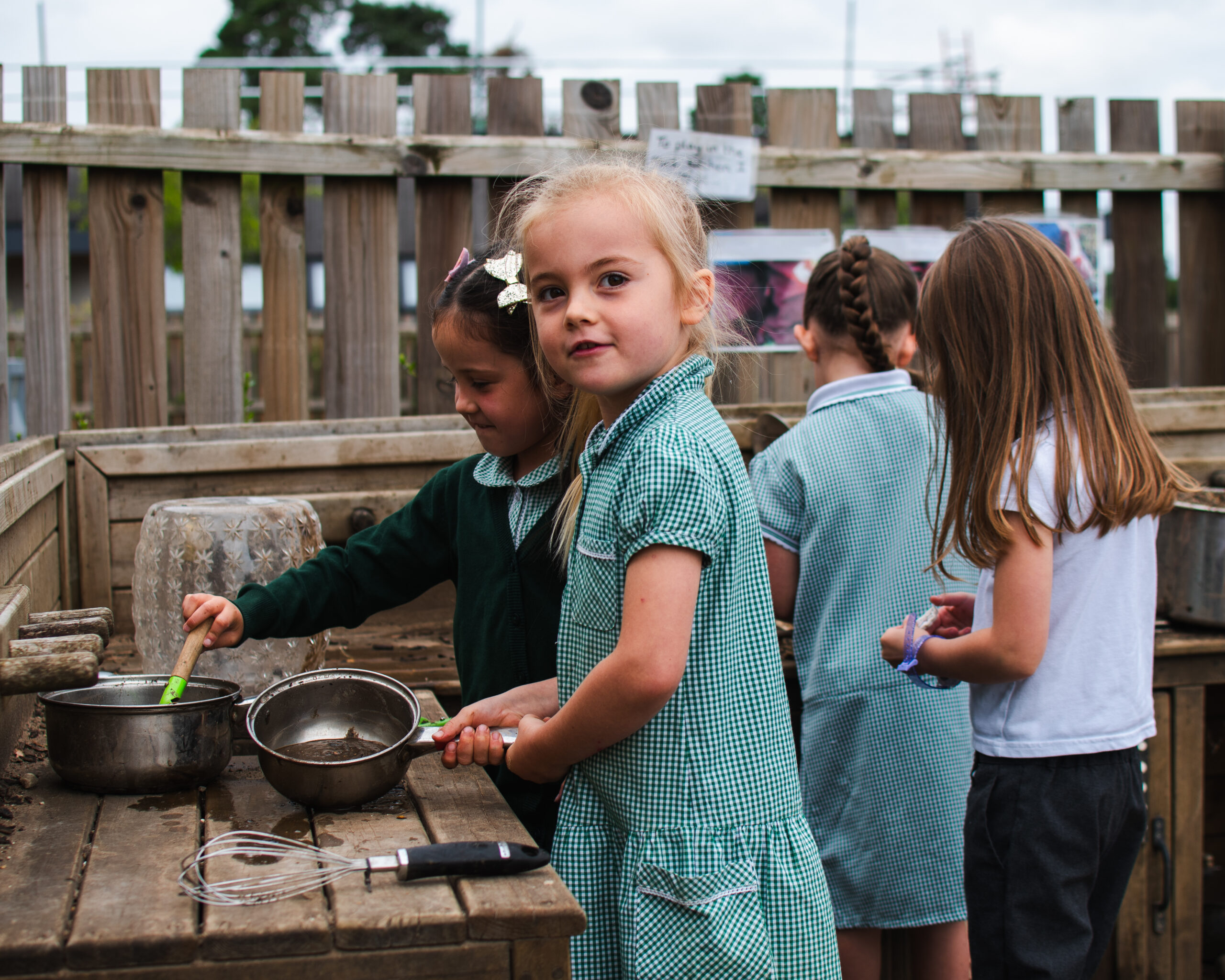 A child playing in an outdoor kitchen smiling at the camera