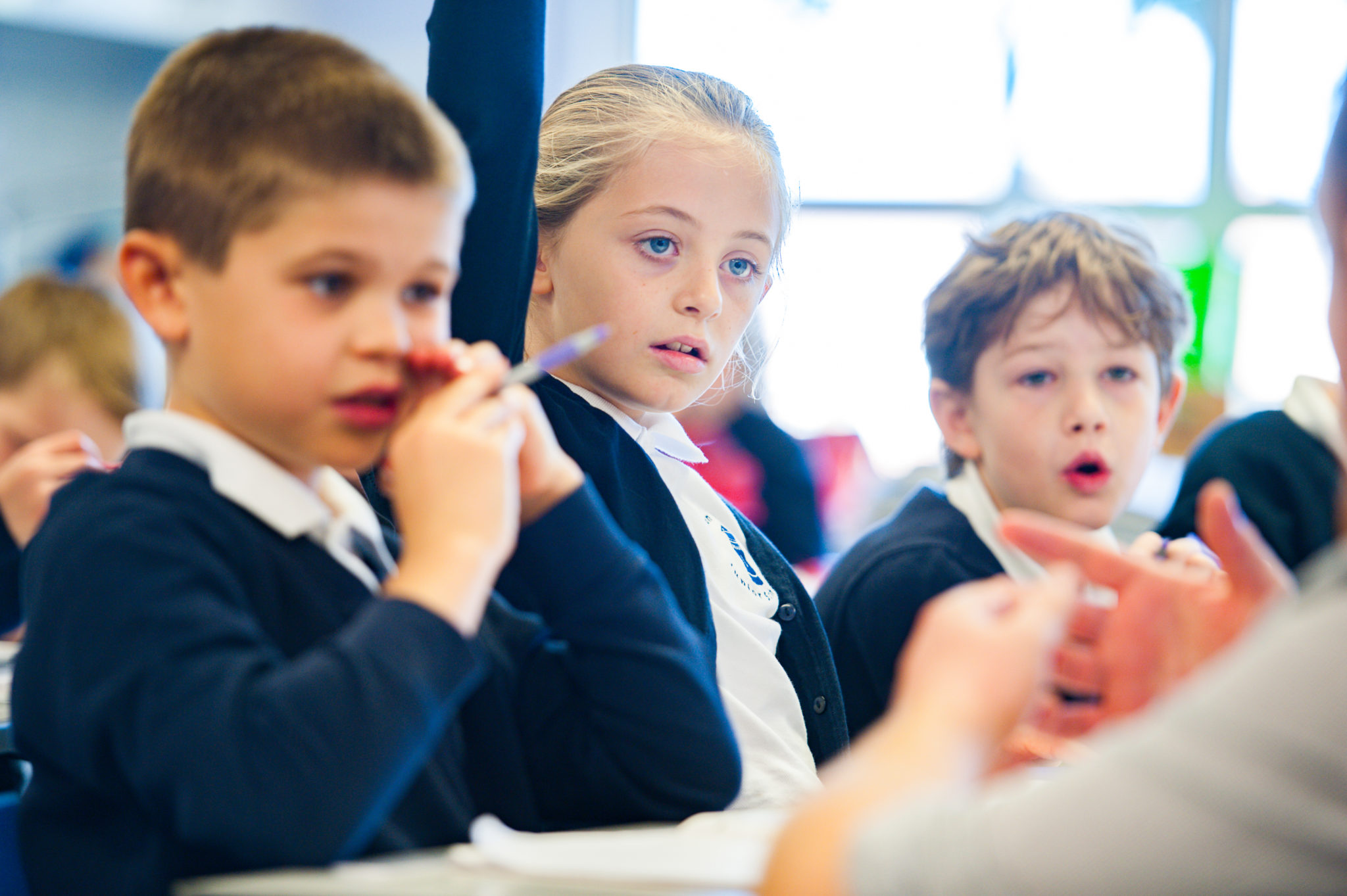 Three pupils sitting at a desk, one has their hand up