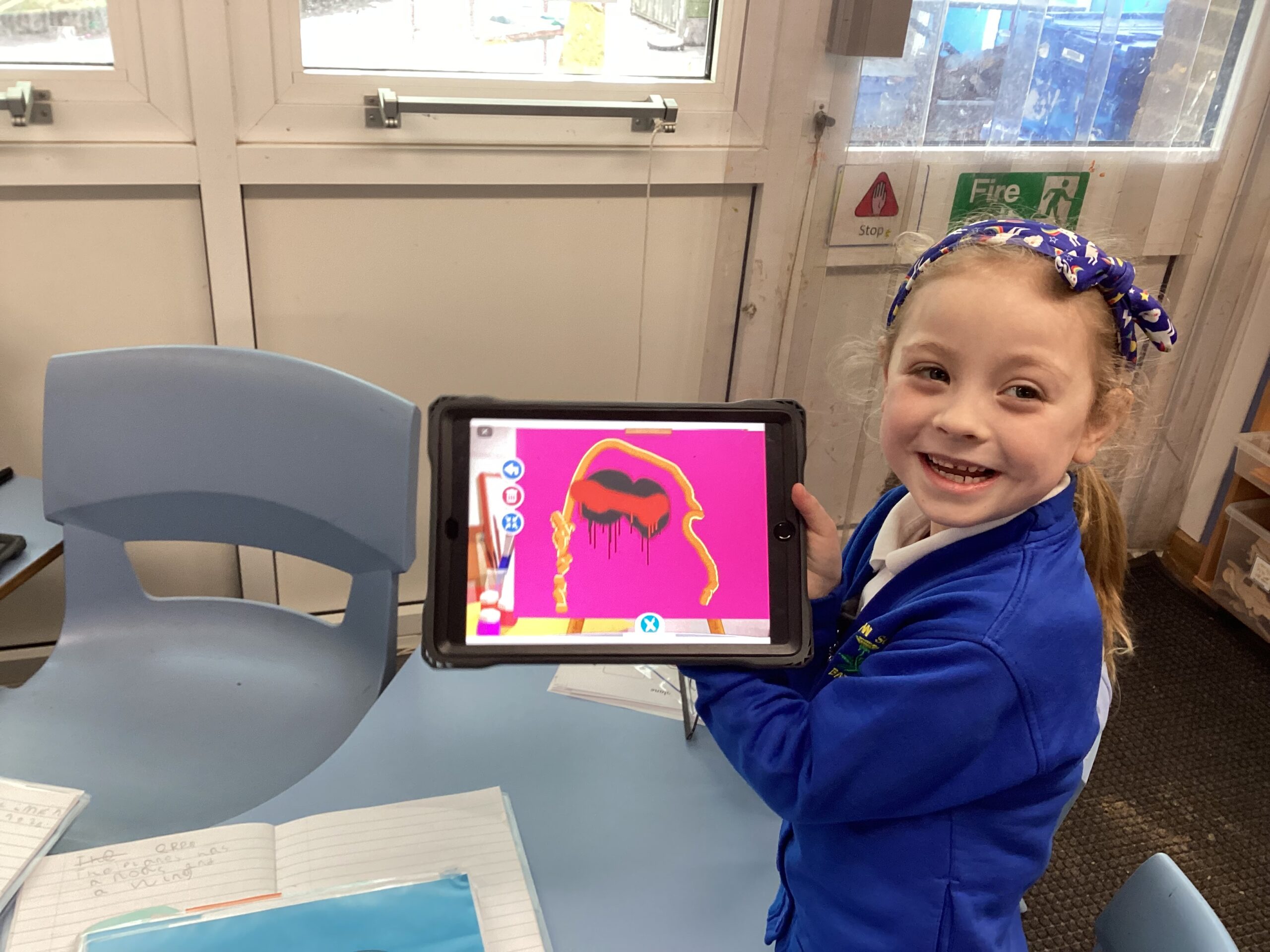 A child holding up an image with a drawing featured on the screen