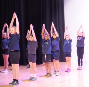 A group of children on stage with their arms above their heads