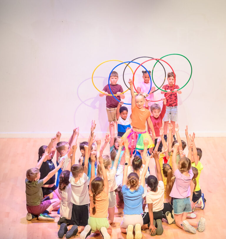 A group of children performing on stage holding hula hoops with one child lifted up and cheering