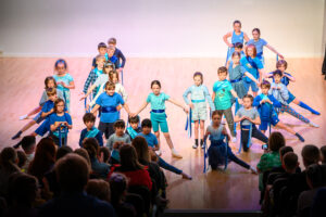 A group of children performing a dance with blue ribbons