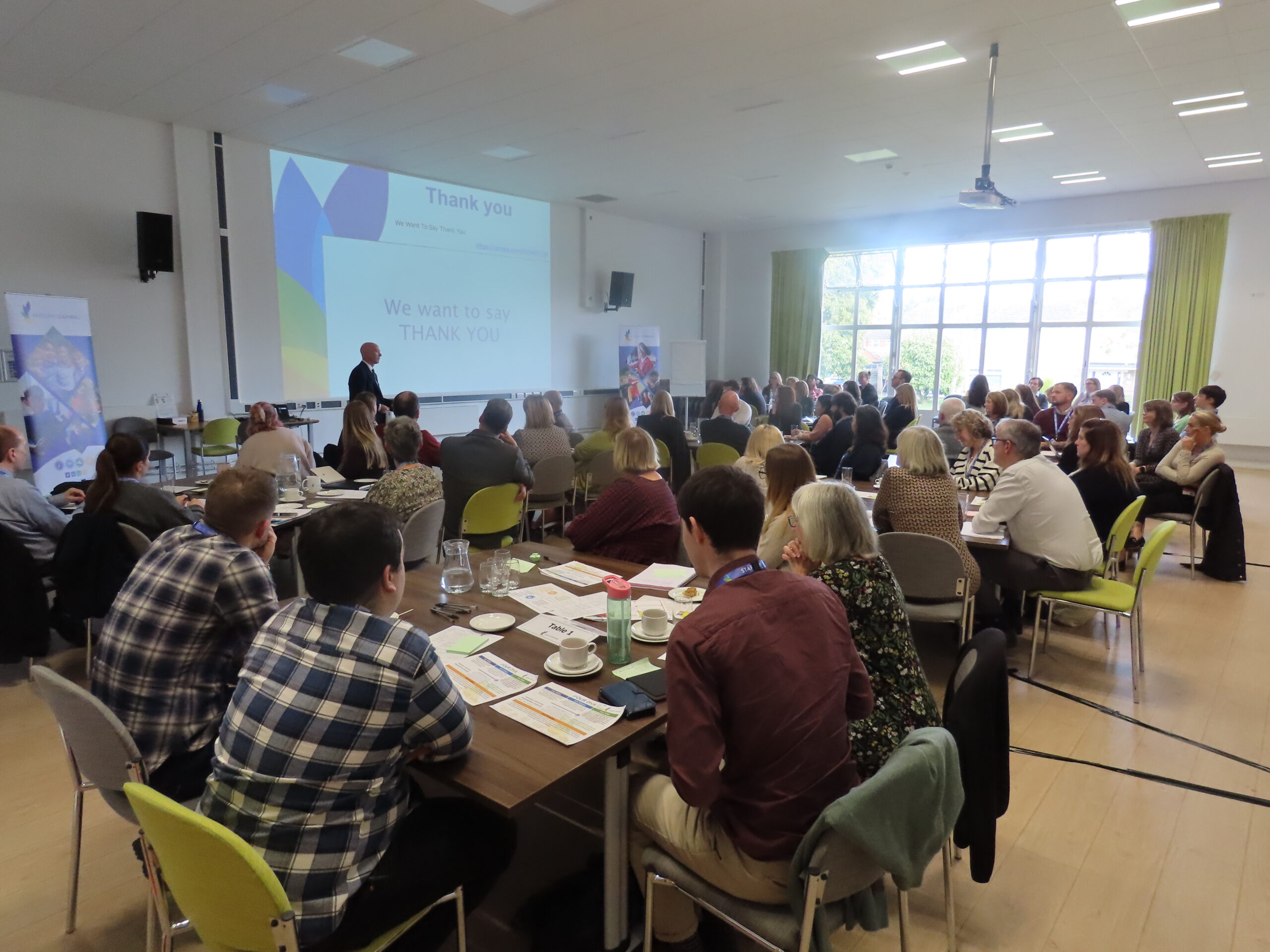 A group of people sitting at a number of tables watching a presentation