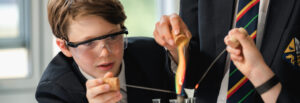 A pupil wearing safety glasses is placing a stick into a Bunsen burner