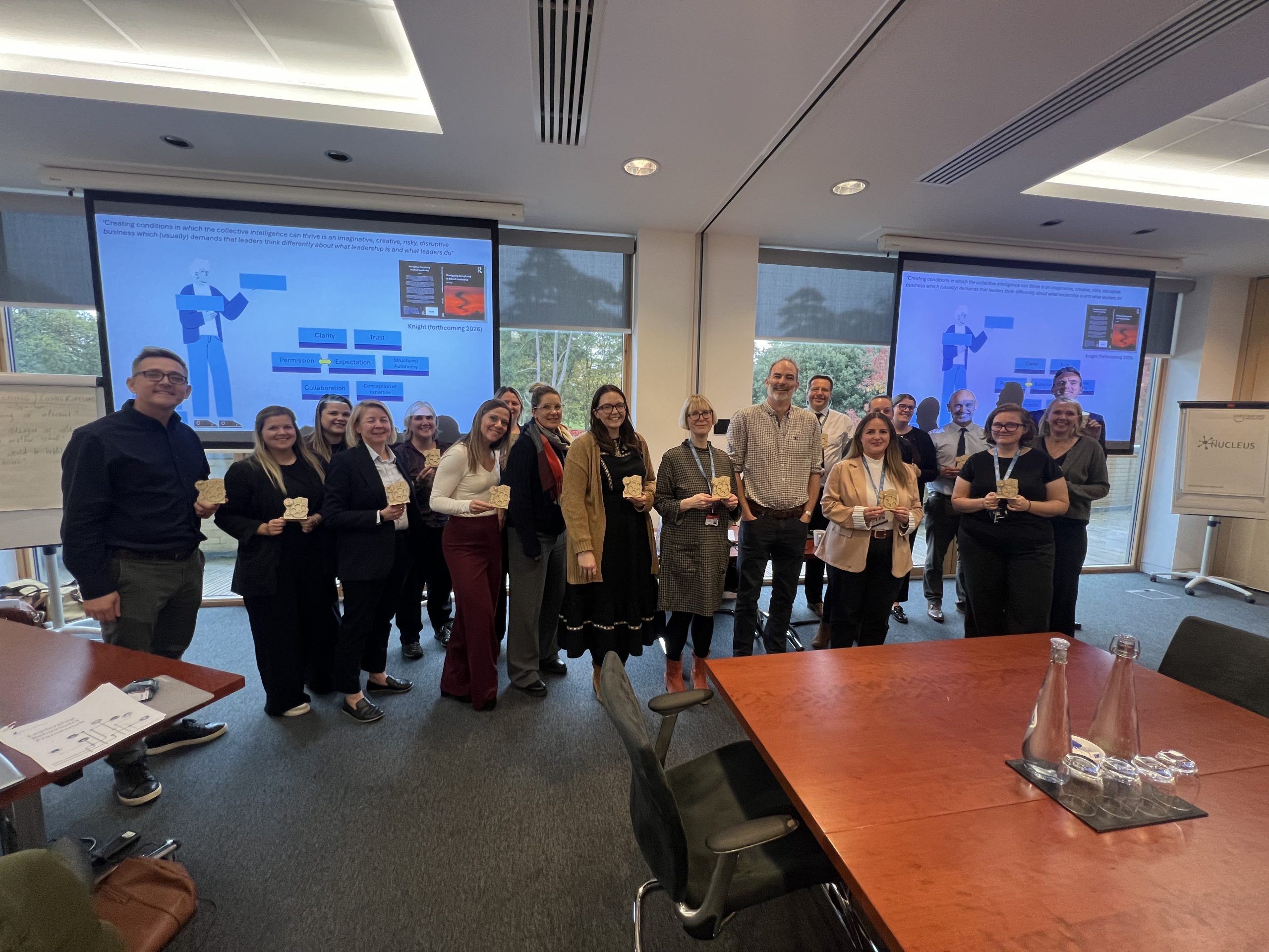A large group of adults are standing in a room in front of two projector screens.